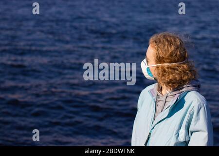 Blonde woman in medical respiratory face mask side view on blurry background with water. Copy space for text on healthcare issue Stock Photo