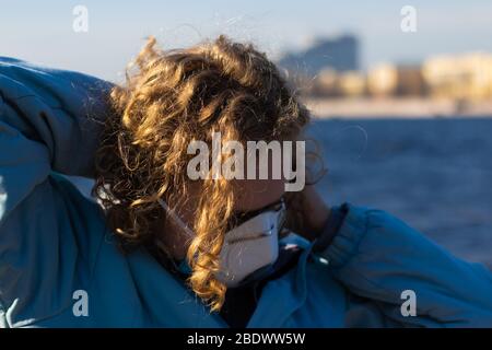 Close-up of face of girl with curly blonde hair. Young woman puts on a medical mask to protect against viruses and bacteria on the street. Copy space Stock Photo