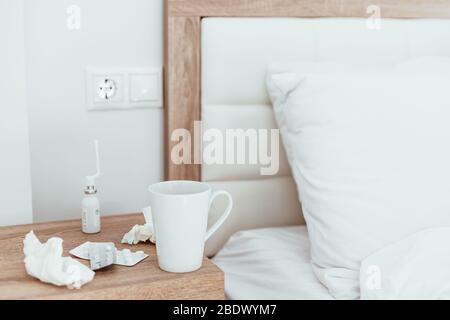 Medicines, pills, nose drops, tissues and hot drink cup on bedside table in modern apartments. Being sick, unwell, flu, illness symptoms. Coronavirus Stock Photo