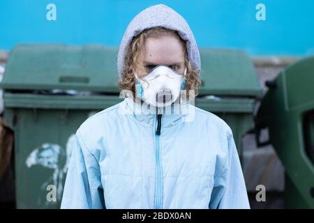 Girl in the hood and a protective mask on her face looks at the camera. Garbage and devastation in the background. The concept of environmental Stock Photo