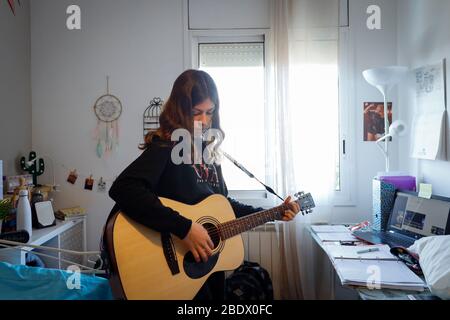 Teenage girl playing the guitar in her bedroom during Covid19 confinement in Catalonia, Spain Stock Photo