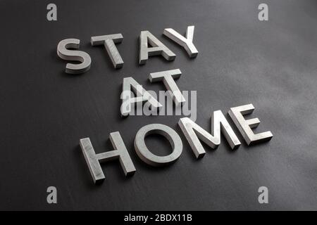 the words stay at home laid with silver metal letters on matte black background in diagonal perspective, slanted full frame view Stock Photo
