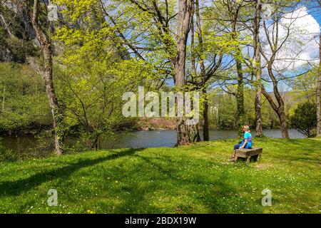 Solitary female sat on stone bench by River Ariege, Ornolac Ussat les Bains, Ariege, French Pyrenees, France Stock Photo