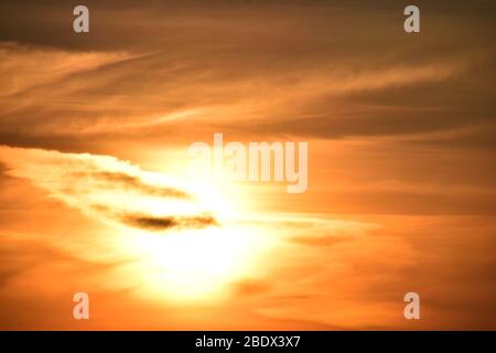 Setting sun set in swath of red and orange hued cloud formations, giving an unearthly appearance. Stock Photo