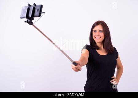 Happy young beautiful woman taking selfie with phone on selfie stick Stock Photo