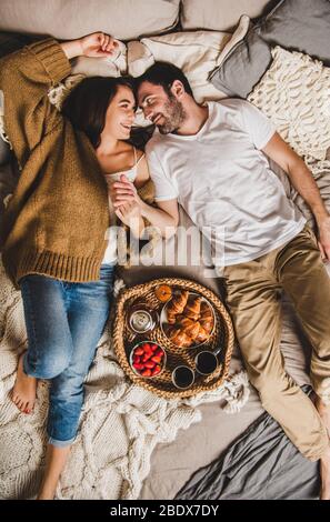 Happy smiling couple having breakfast in bed and holding hands Stock Photo