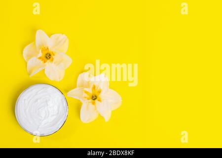 Flowers head of daffodil and cosmetic cream in jar on bright yellow background. Skin care concept with natural creams. Top view. Flat lay. Copy space. Stock Photo