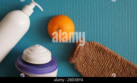 Lotion, orange, shower sponge and anti-cellulite massager on a blue background. Healthy and beautiful skin concept. Stock Photo