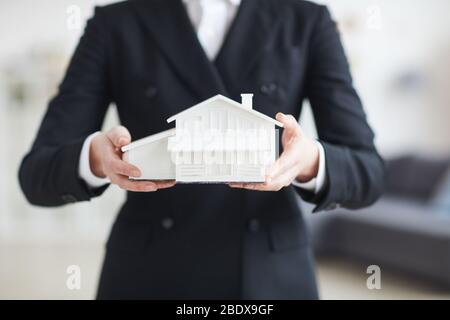 Close-up of real estate agent in black suit holding model of the house in her hands Stock Photo