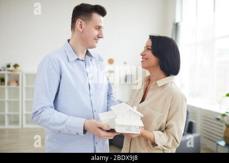 Young couple holding model of the house and smiling to each other while standing in the living room at home Stock Photo
