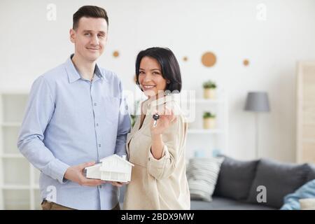 Portrait of young couple holding model of the house and keys from their new home they standing and smiling at camera Stock Photo
