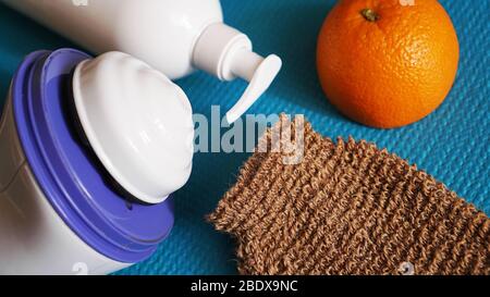 Lotion, orange, shower sponge and anti-cellulite massager on a blue background. Healthy and beautiful skin concept. Stock Photo