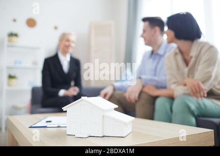Close-up of model of new house on the table with young couple and real estate agent in the background at home Stock Photo