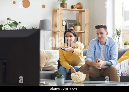 Happy young couple sitting on sofa and spending their leisure time at home they watching TV Stock Photo
