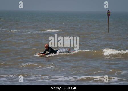 A man on top of a surf board enjoys the sea in Margate, Kent during the Easter bank holiday weekend, as the UK continues in lockdown to help curb the spread of the coronavirus. Stock Photo