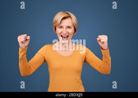 Middle aged woman raised fists up and rejoice loud Stock Photo