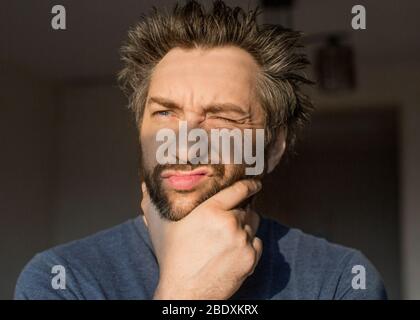 Funny man after waking scratches his beard, looking at the morning sun. Close upportrait. Stock Photo