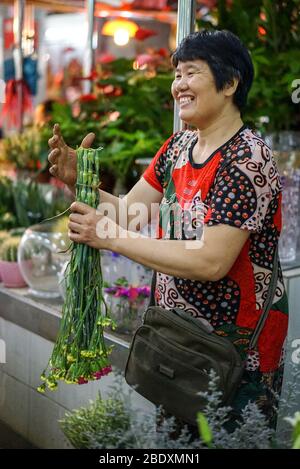 Happy Asian smiling woman sells beautiful fresh flower bouquets on the floral market Stock Photo