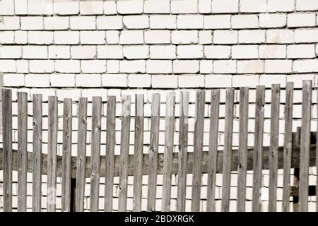 Old grey boardwalk wooden fence with parallel planks in front of a white brick wall on a bright sunny day. A concept of rural life with space for text Stock Photo