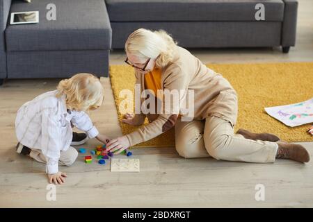 Grandmother sitting on the floor with little boy and helping him in educational games they are at home Stock Photo