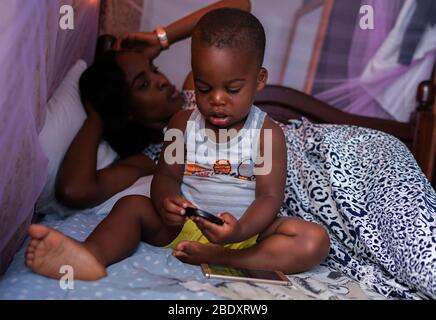 Kampala, Uganda - June 15th, 2017: a portrait of an African woman with her son while they were resting in the afternoon in  the bedroom on a bed Stock Photo