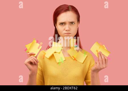 Serious looking young girl frown, covered with stickers listens information attentively. Young indignant, perturbed girl has long red hair, wears yell Stock Photo