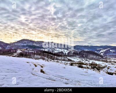 Scenic mountanous landscape with snowy slopes, snow covered mountain tops and clouds lit up by the sunset in the Carpathian Mountains of Romania, beau
