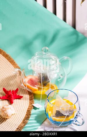 Creative summer composition from wide-brimmed hat, red starfish, shell and glass set with ingredients for making fresh fruit cold tea drink on a duoto Stock Photo