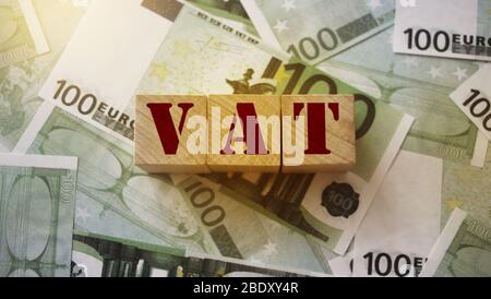VAT on wooden alphabet cubes with 100 euro banknotes around. Selective focus . Taxes and fees financial concept Stock Photo