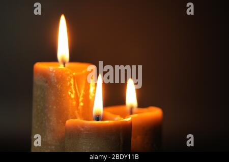 Group of three brown burning candles on a black background close-up. Concept of comfort,romance,mystic,occultism,religion,a symbol of memory.Copy