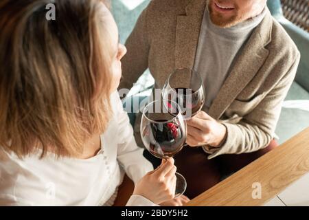 Young romantic dates clinking with glasses of red wine while sitting by table in restaurant and making toast for their relationship Stock Photo