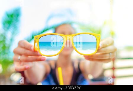 Young woman is holding sunglasses in her hand against the background of palms. Stock Photo