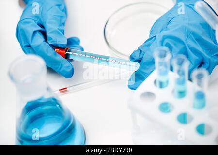 scientist in protective gloves holds tube with liquid and written word covid-19 Stock Photo