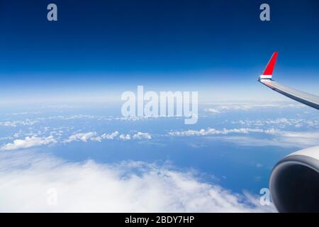 View from window of airliner wing and engine above clouds and Atlantic ocean, with blue sky and horizon. Depicts airline business travel Stock Photo