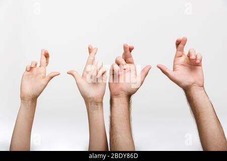 Closeup photo of a man's and woman's raised hands isolated over white wall background showing hopeful please fingers crossed gesture. Stock Photo