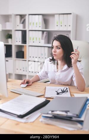 Young female accountant or financial analyst in formalwear keeping hand on mouse while scrolling through online information on screen Stock Photo