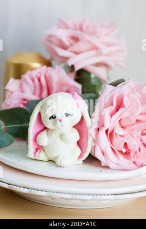 White chocolate bunny with pink ears with roses and golden candle on the background Stock Photo