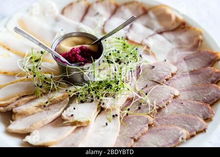 Meat, mustard, horseradish, greens on a plate. Slices of meat on a white plate. Stock Photo