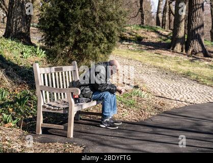 Berks County, Pennsylvania, USA-March 13, 2020: Senior man sits on park bench alone in public park. Stock Photo