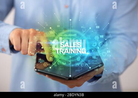 Businessman holding a foldable smartphone with SALES TRAINING inscription, new business concept
