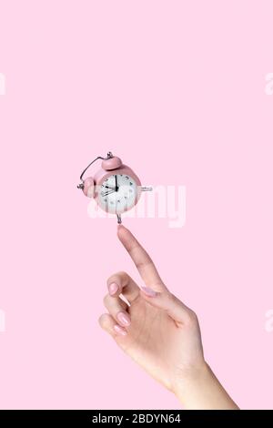 Alarm clock balancing on womans hand on pink background Stock Photo