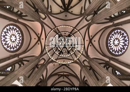 Ceiling of a church with arcades, rose windows and a large hanging candle lamp. Religion concept Stock Photo