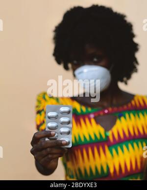 Virus Crisis around the world: African Woman Upper Body Shot with Mask and Medicament Pills Stock Photo