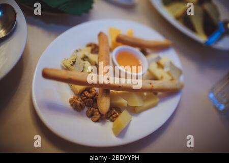 Cheese platter on a white plate with bread sticks and honey. Stock Photo