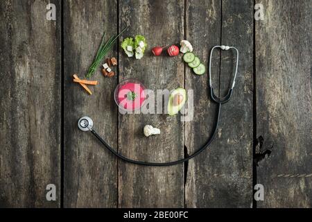 Importance of healthy eating for overall health - various fresh vegetables and medical stethoscope placed over rustic wooden background to form a smil Stock Photo