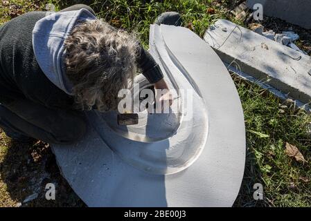 Top view of an artist using chisel and a mallet to carve in white marble stone. Stock Photo