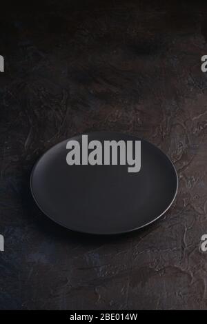 Empty black plate on dark textured background, angle view Stock Photo