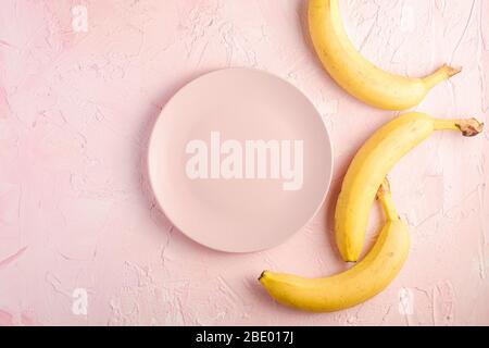 Banana fruits with empty pink plate on pink textured background, top view copy space Stock Photo