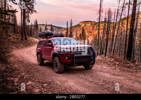 Desert road trip with red pickup truck camper and overland equipment. Stopped on red gravel road looking out over burnt forest and red rock formations Stock Photo