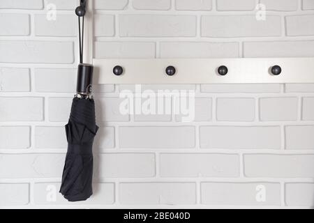 Black short umbrella hanging on hanger in white hallway interrior Stock Photo